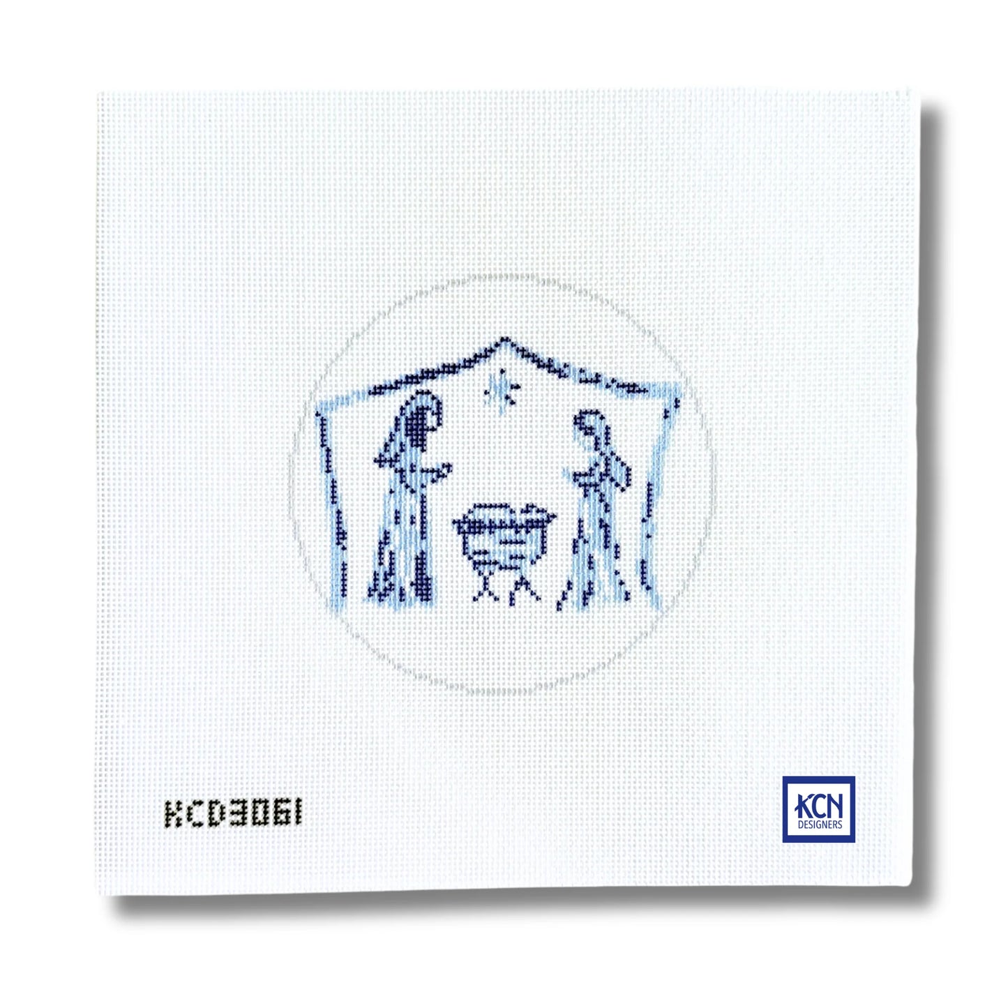 A square white needlepoint canvas featuring a blue embroidered nativity scene with Mary, Joseph, baby Jesus in a manger, and a star. The canvas has the printed code 'KCD3061' in the bottom-left corner and a blue 'KCN' logo in the bottom-right corner.