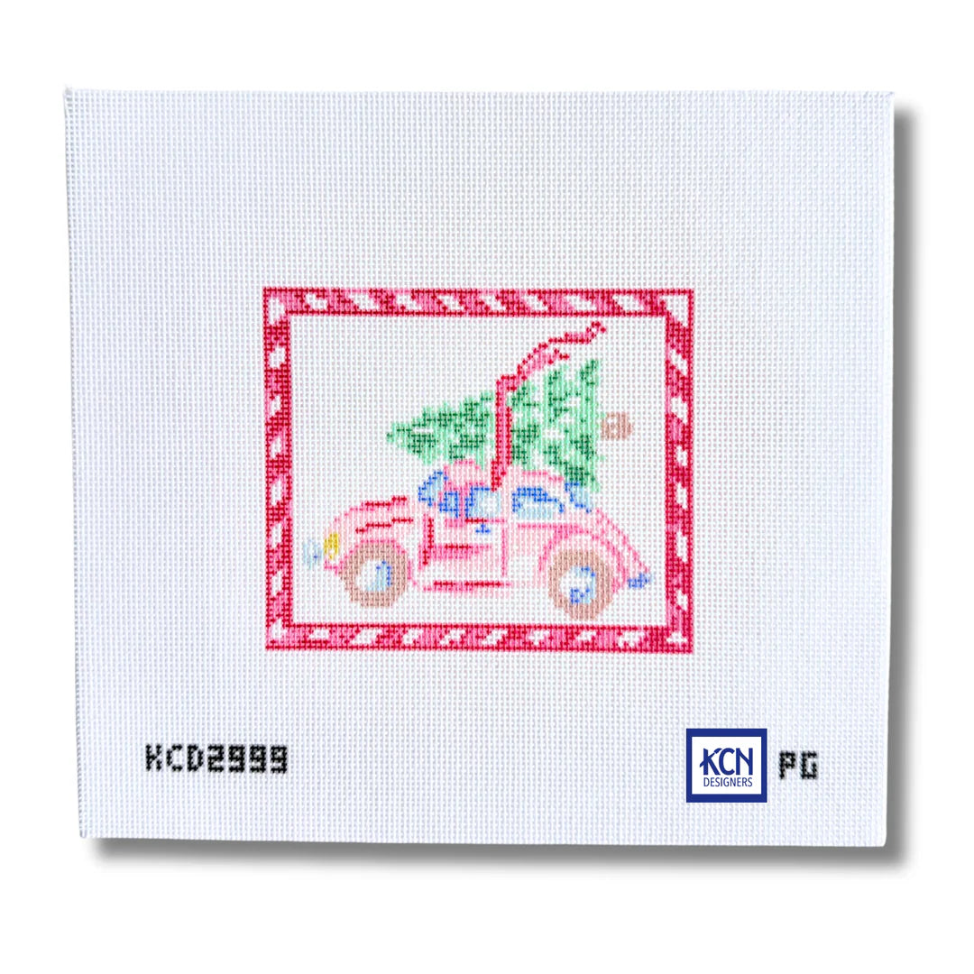 A square white needlepoint canvas featuring a cross-stitched style illustration of a pink car carrying a green Christmas tree, framed by a red patterned border. The canvas shows printed text at the bottom including 'KC02999' and a 'KCN Needlepoint' logo.