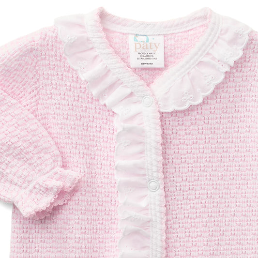 A close-up of a baby cardigan in light pink and white. The cardigan features a textured waffle knit body, a white ruffled collar, a ruffled button placket, and a ruffled sleeve cuff.