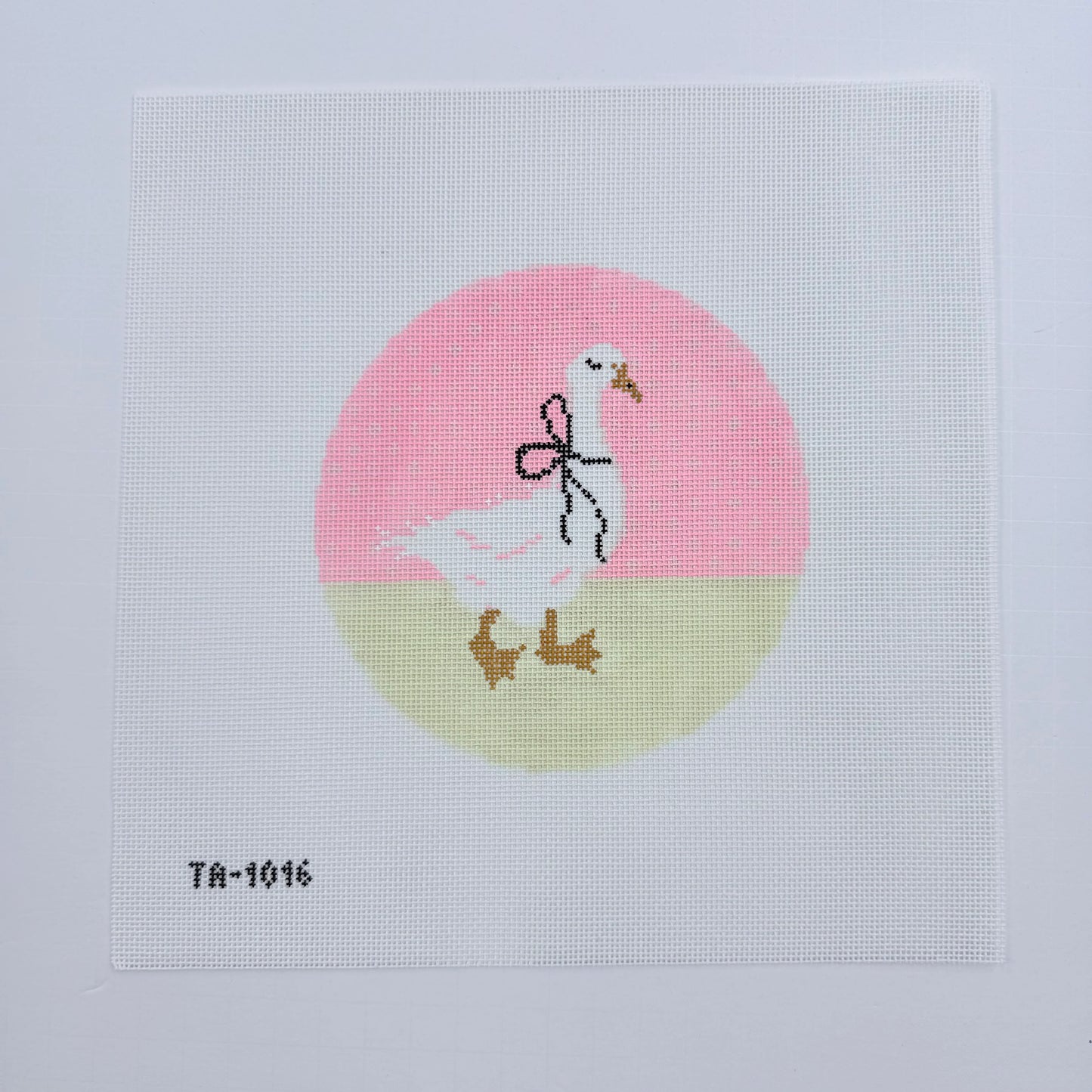 Cross-stitched design of a stork with baby shoes and socks on a pink and beige circle background.
