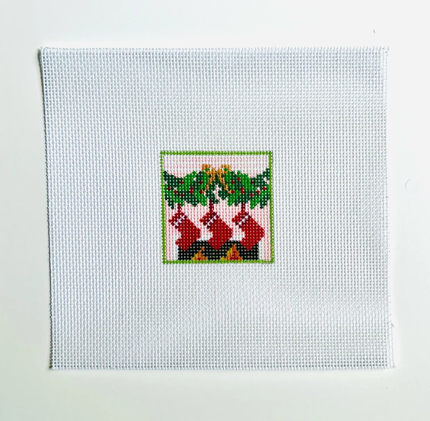 Cross-stitched design of stockings hanging by a fireplace on white fabric.