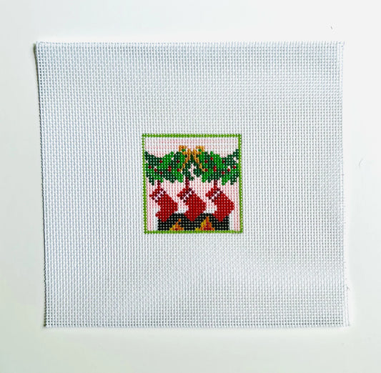 Cross-stitched design of stockings hanging by a fireplace on white fabric.