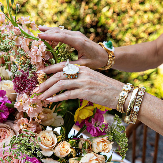 Close-up of hands with gold rings and bracelets on a floral background