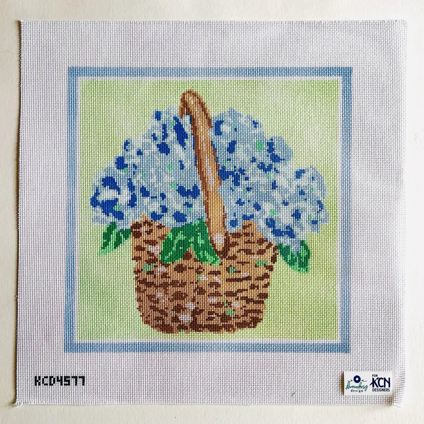 Cross-stitched design of a basket with blue flowers on fabric.