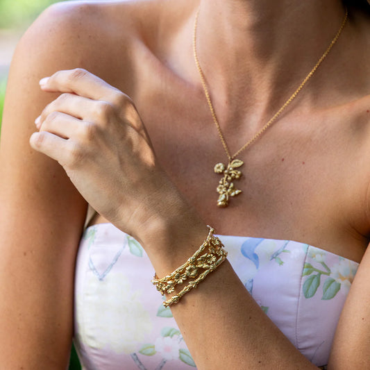 Person wearing a gold necklace and bracelet with a floral-patterned top.