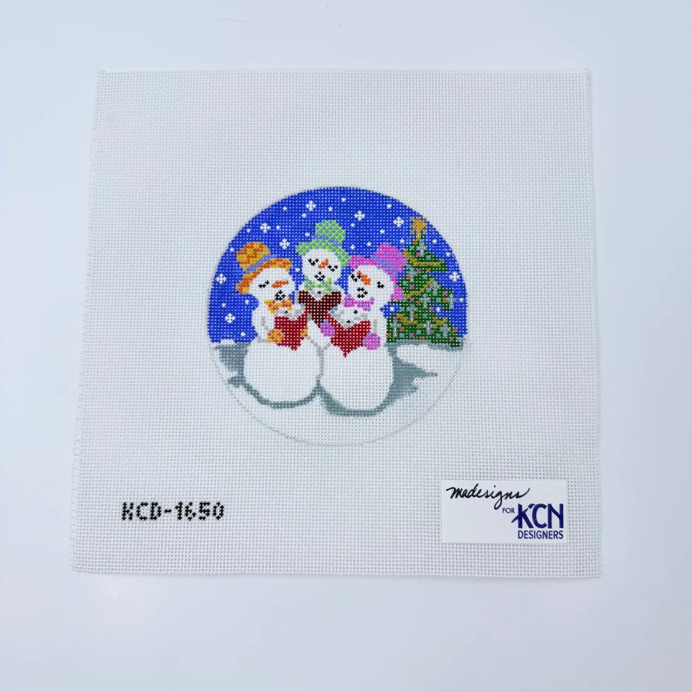 Needlepoint Canvas with round painting of 3 snowmen caroling, and Christmas tree in background.
