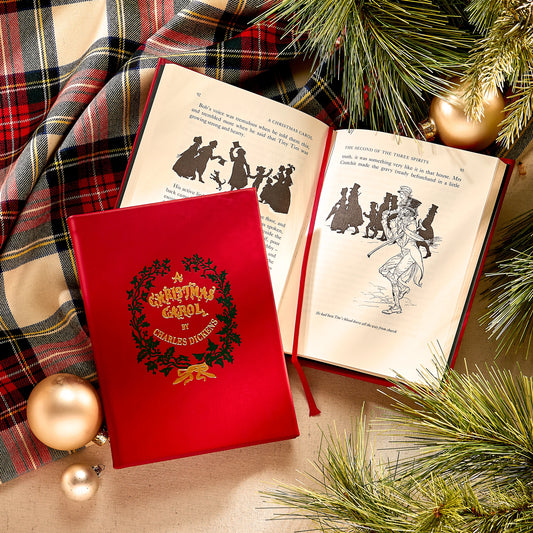 Red book cover of 'A Christmas Carol' by Charles Dickens with open book featuring silhouettes, surrounded by Christmas decorations.