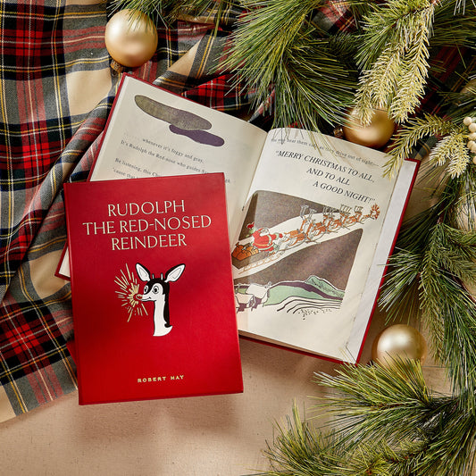 Red book titled 'Rudolph the Red-Nosed Reindeer' on a wooden surface with Christmas decorations.