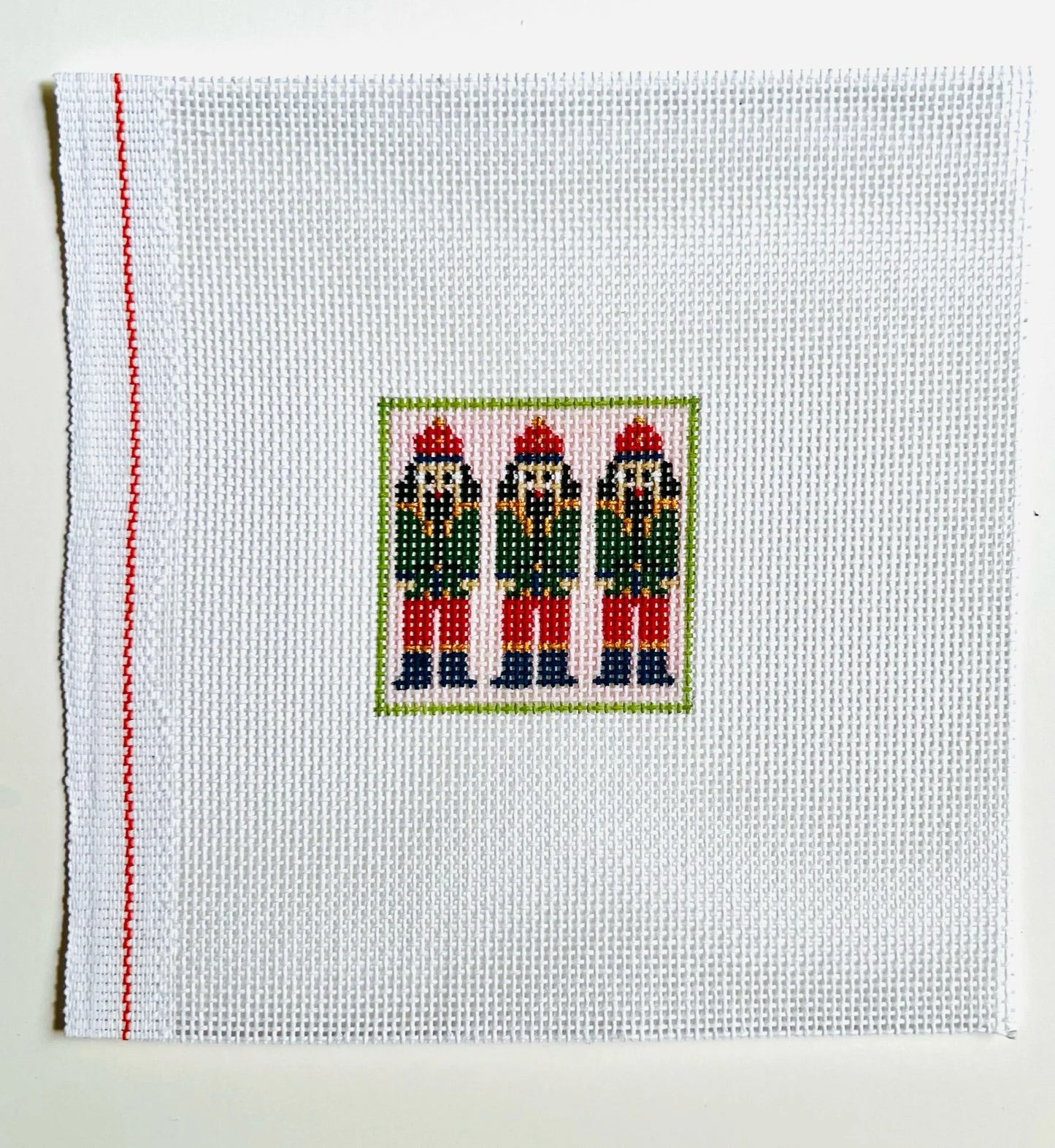 Cross-stitched design of three nutcrackers on a white fabric background