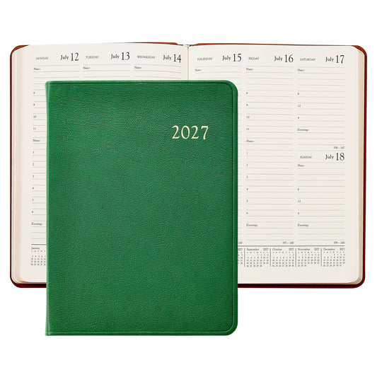 A 2027 daily planner with a textured navy blue crocodile skin cover, shown in front of an open view of the same planner displaying its daily layout pages.