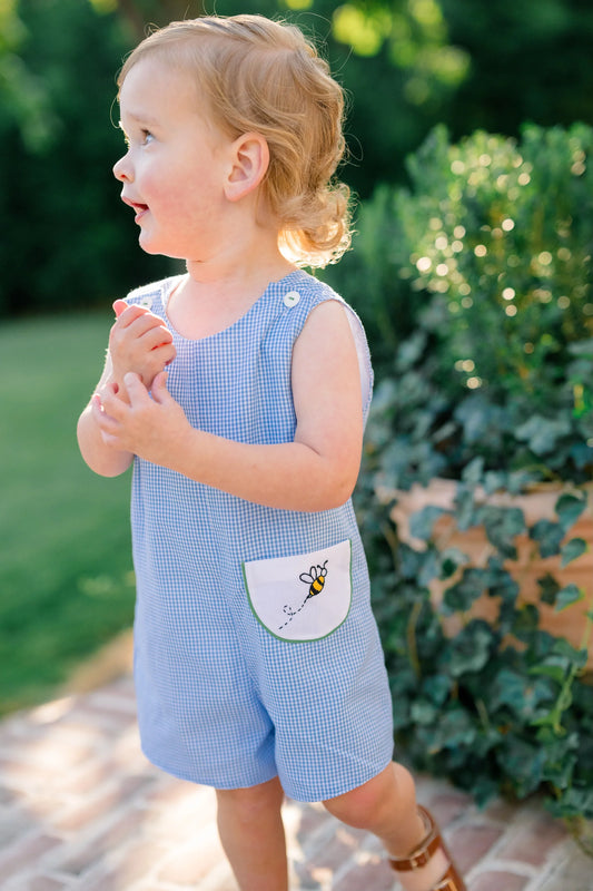 Child wearing a blue checkered romper with a pocket design outdoors.