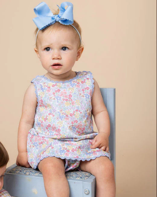 Baby wearing a floral dress and blue headband sitting on a box against a beige background