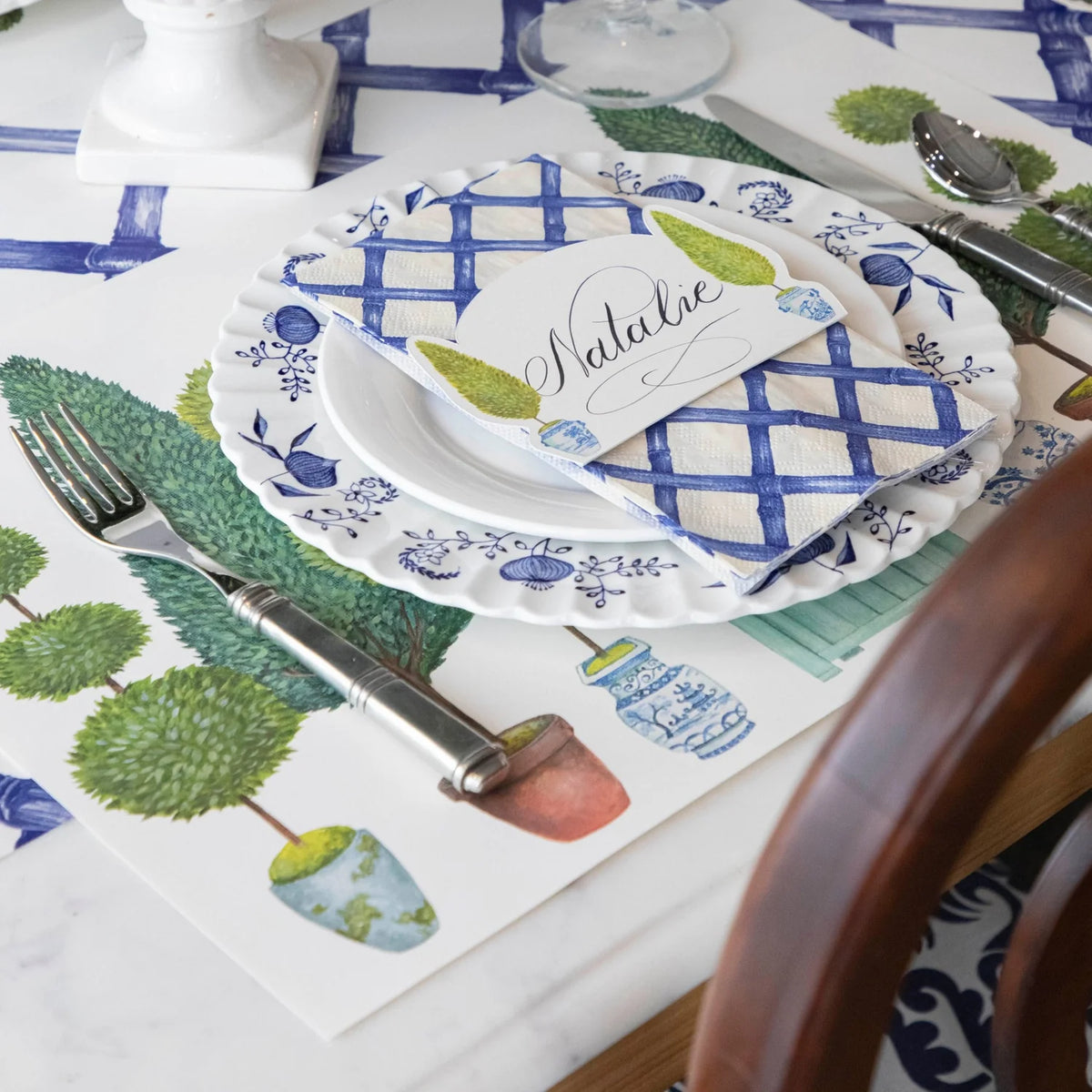 Table setting with blue and white checkered plates, green leafy patterns on placemats, and silverware.