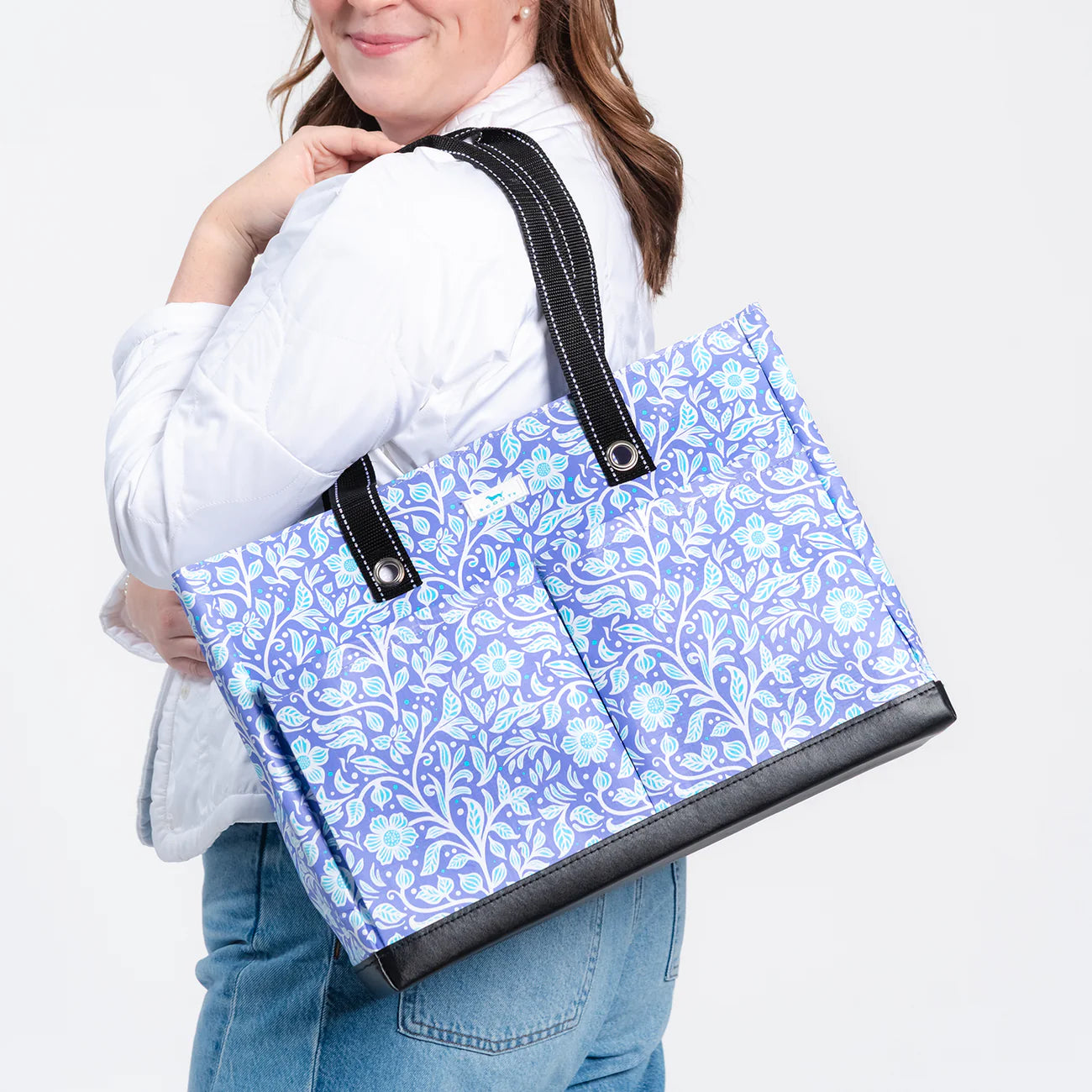 Person holding a blue floral-patterned tote bag with black accents.