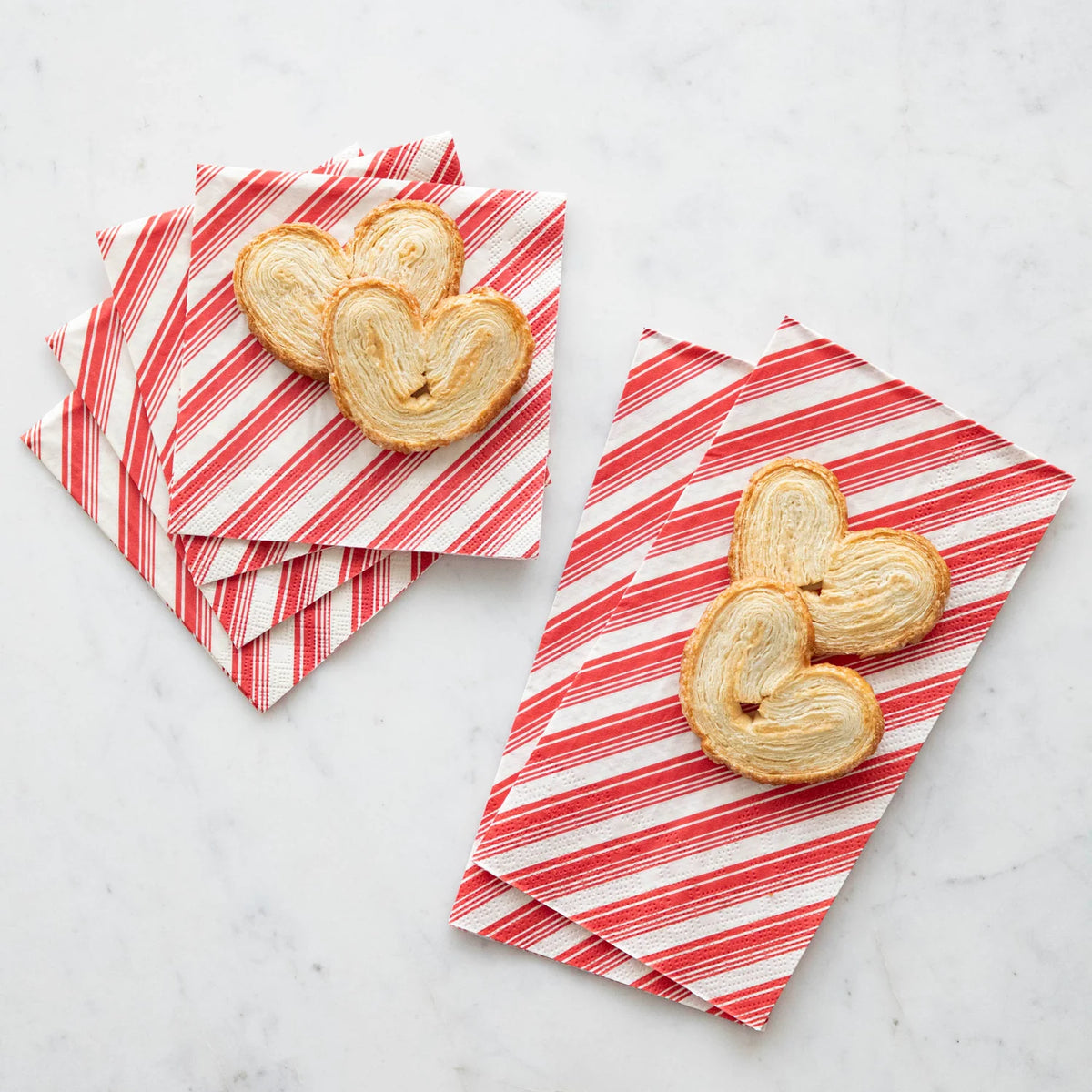 Heart-shaped pastry cookies arranged on red-and-white striped napkins on a light marble surface.