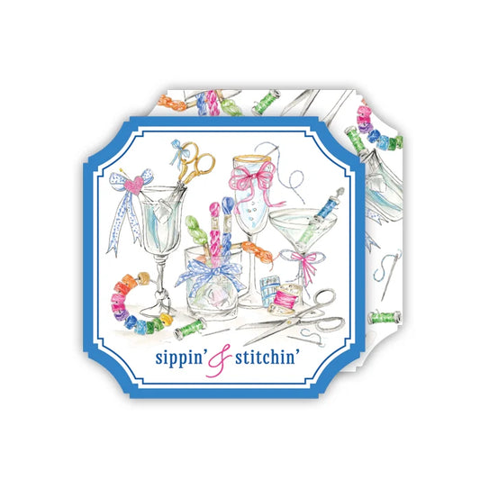 A square decorative card or print with rounded corners, featuring a blue border and a watercolor-style illustration of sewing and cocktail-themed items such as scissors, glasses, bows, and colorful thread spools. The text 'sippin' & stitchin'' appears at the bottom.