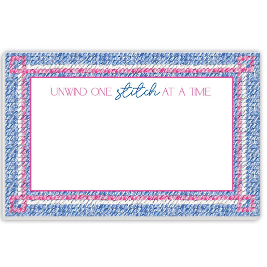 A square white card or coaster with a decorative border made of blue and pink stitched-look texture. The top center reads 'UNWIND ONE stitch AT A TIME' in pink and blue script, with a large blank white space below.