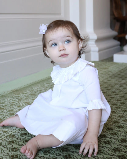 Young child in a white outfit sitting on a patterned rug.