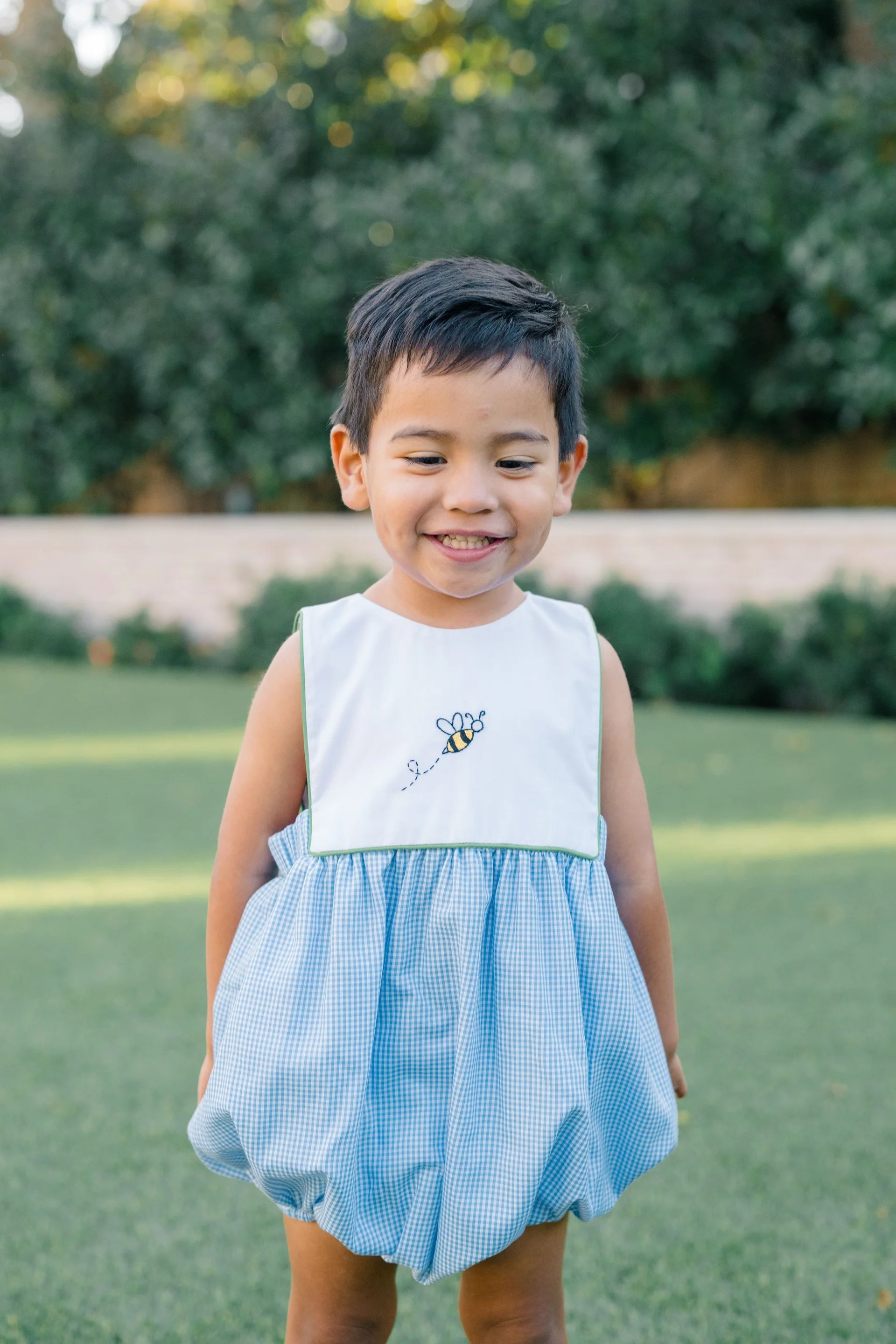 Child wearing a white top with a bee design and a blue checkered skirt outdoors.