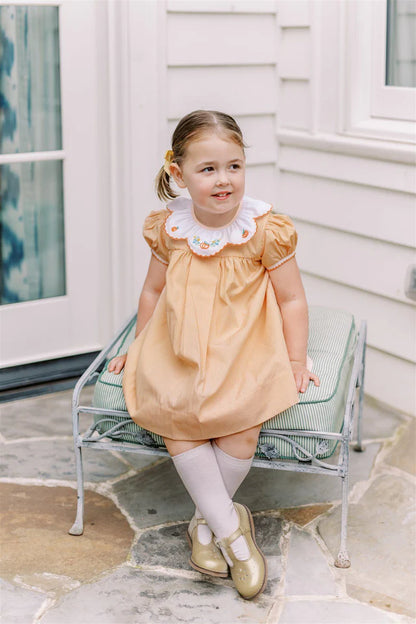 Young girl in a peach dress sitting on a small bench outside a house.