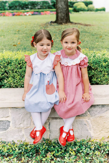 Two young girls in dresses sitting on a stone wall outdoors.