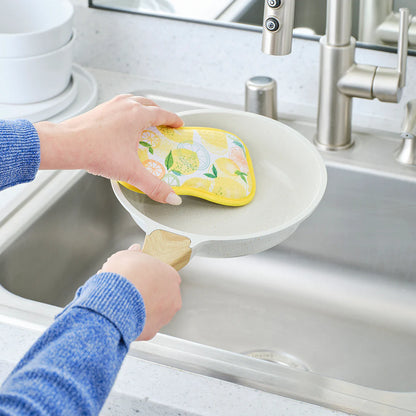 Person holding a yellow sponge over a white dish rack in a kitchen sink.