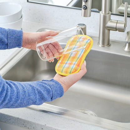 Person cleaning a glass with a colorful dishcloth in a kitchen sink.