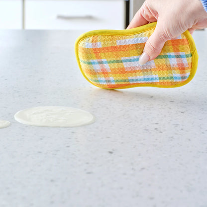 Hand holding a colorful potholder over a marble countertop with a small spill.
