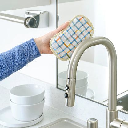 Person using a kitchen faucet with a colorful hot pad on a kitchen counter.