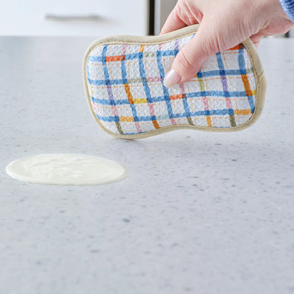 Hand holding a checkered cleaning pad over a spill on a marble countertop