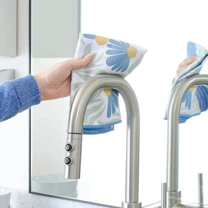 Person cleaning a kitchen faucet with a floral towel