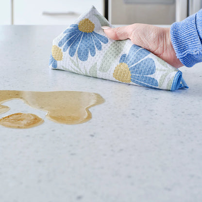 Hand using a floral-patterned cloth to clean up a spill on a countertop.