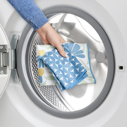 Hand holding a floral towel in front of an open washing machine.