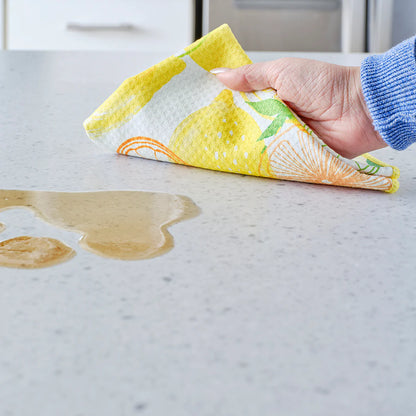 Hand using a colorful cloth to wipe up a spill on a marble countertop.