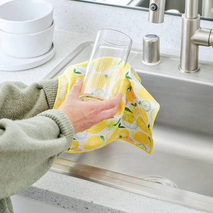 Person drying a glass with a yellow lemon-patterned towel in a kitchen sink.