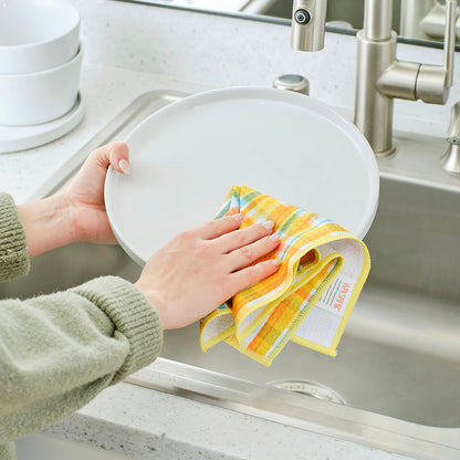 Person drying a white plate with a colorful towel in a kitchen sink.