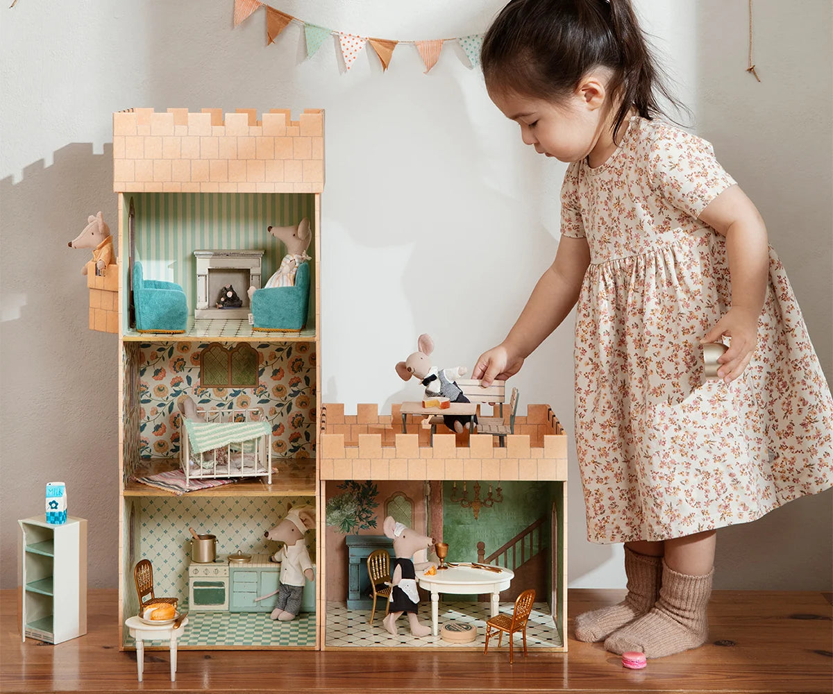 Child playing with a wooden dollhouse set in a room.