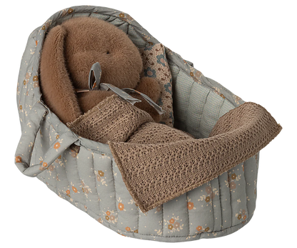 Baby carrier with brown teddy bear and blanket on a white background
