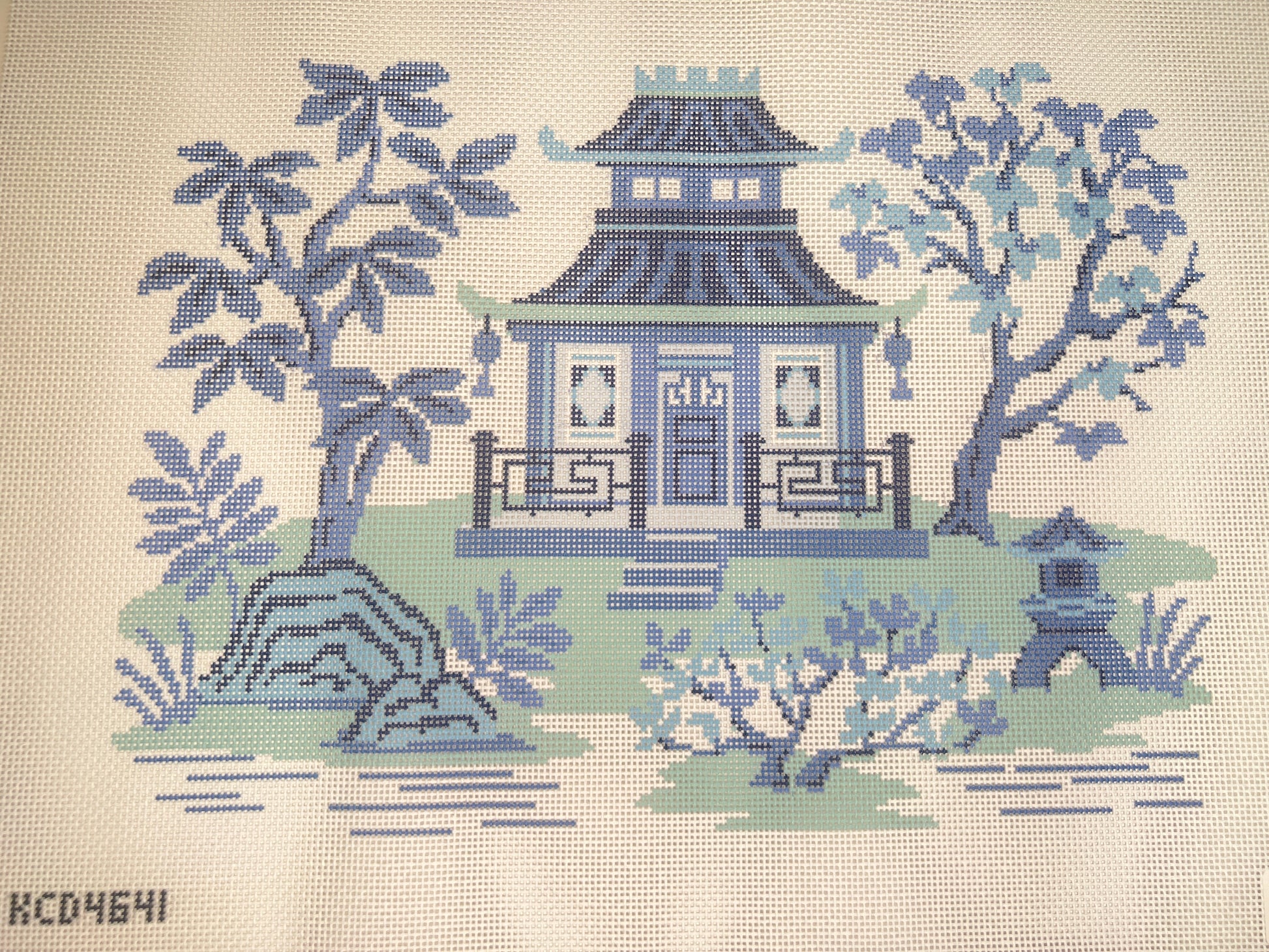 Embroidered design of a blue pagoda with trees and garden elements on a beige background.