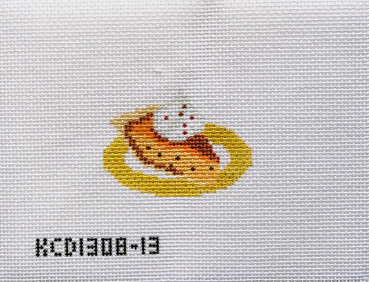 Cross-stitched design of a fish on a plate with 'KCD1308-13' label on fabric background