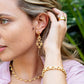 Woman wearing gold jewelry including earrings, necklace, and bracelet with a blurred green background