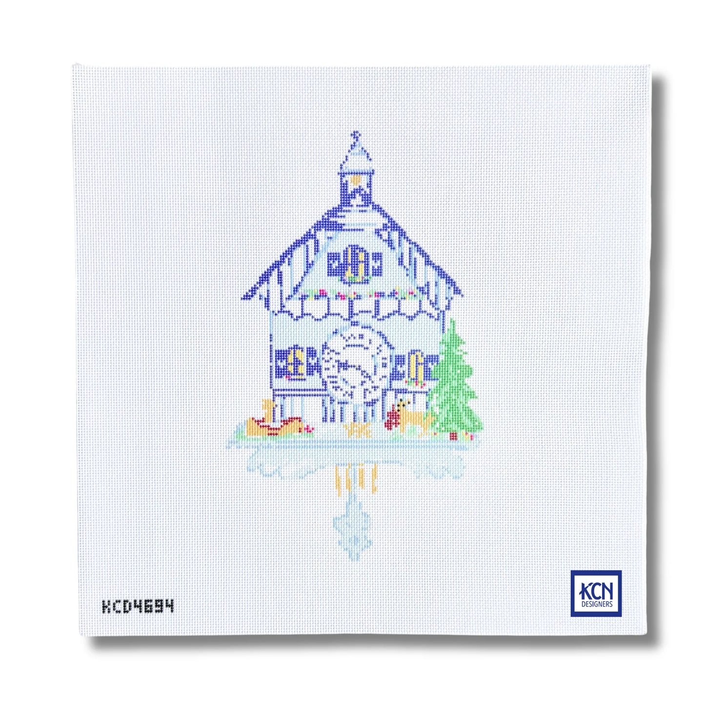 A square white needlepoint canvas featuring a stitched illustration of a traditional Swiss chalet house with a large clock, a green tree, and a reflection in water. The KCN Designs logo is visible in the bottom right corner.