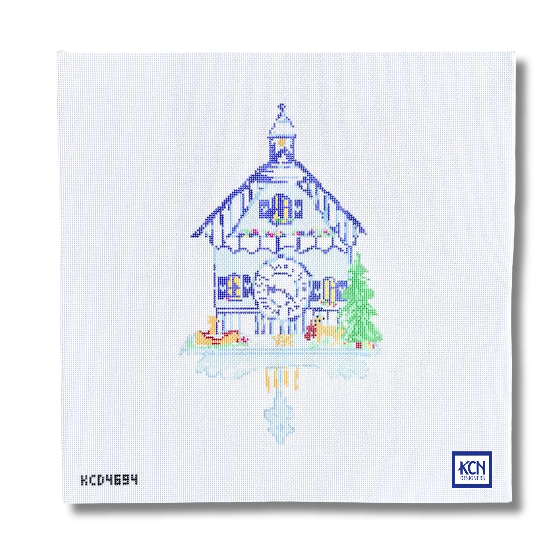 A square white needlepoint canvas featuring a stitched illustration of a traditional Swiss chalet house with a large clock, a green tree, and a reflection in water. The KCN Designs logo is visible in the bottom right corner.