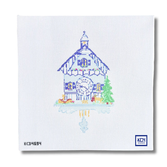 A square white needlepoint canvas featuring a stitched illustration of a traditional Swiss chalet house with a large clock, a green tree, and a reflection in water. The KCN Designs logo is visible in the bottom right corner.