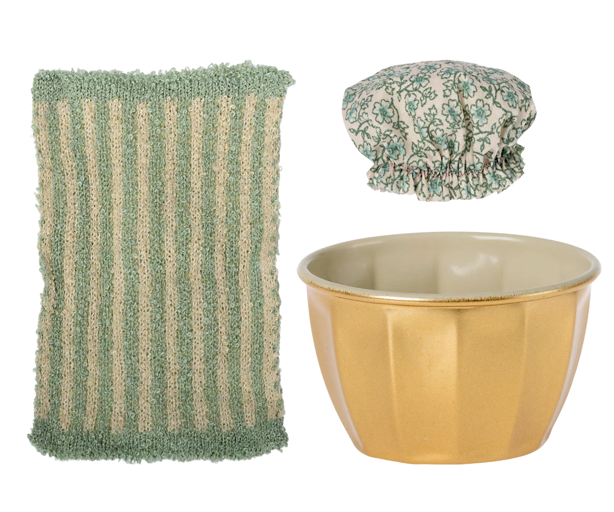 Green scrubber, gold bowl, and floral shower cap on a white background