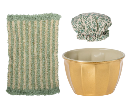 Green scrubber, gold bowl, and floral shower cap on a white background