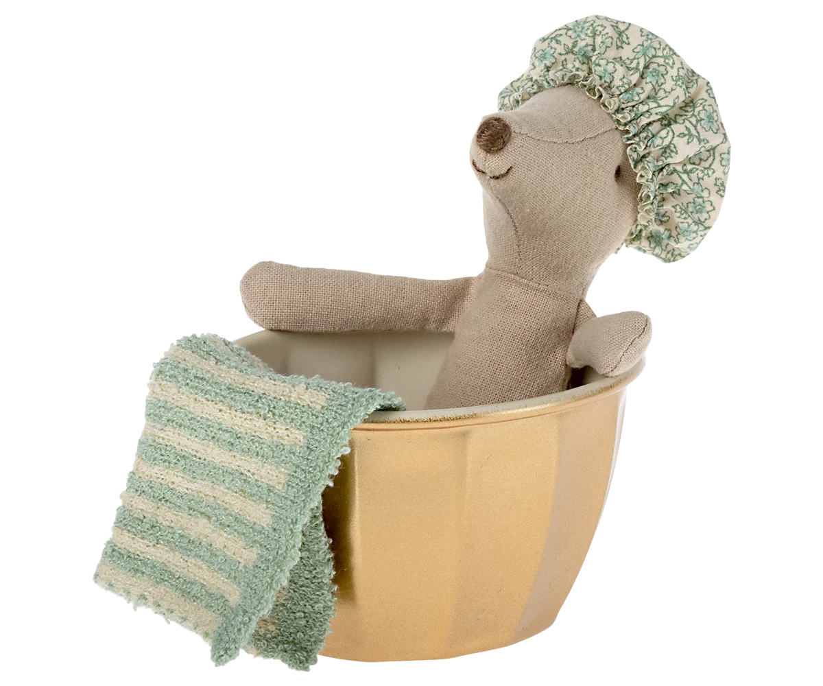 Plush toy bear in a bathtub with a green towel and shower cap on a white background