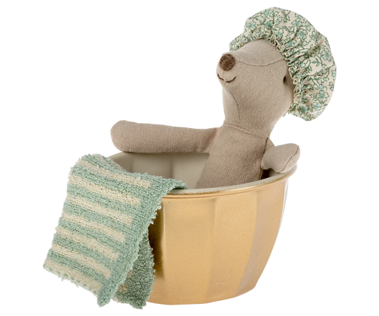 Plush toy bear in a bathtub with a green towel and shower cap on a white background