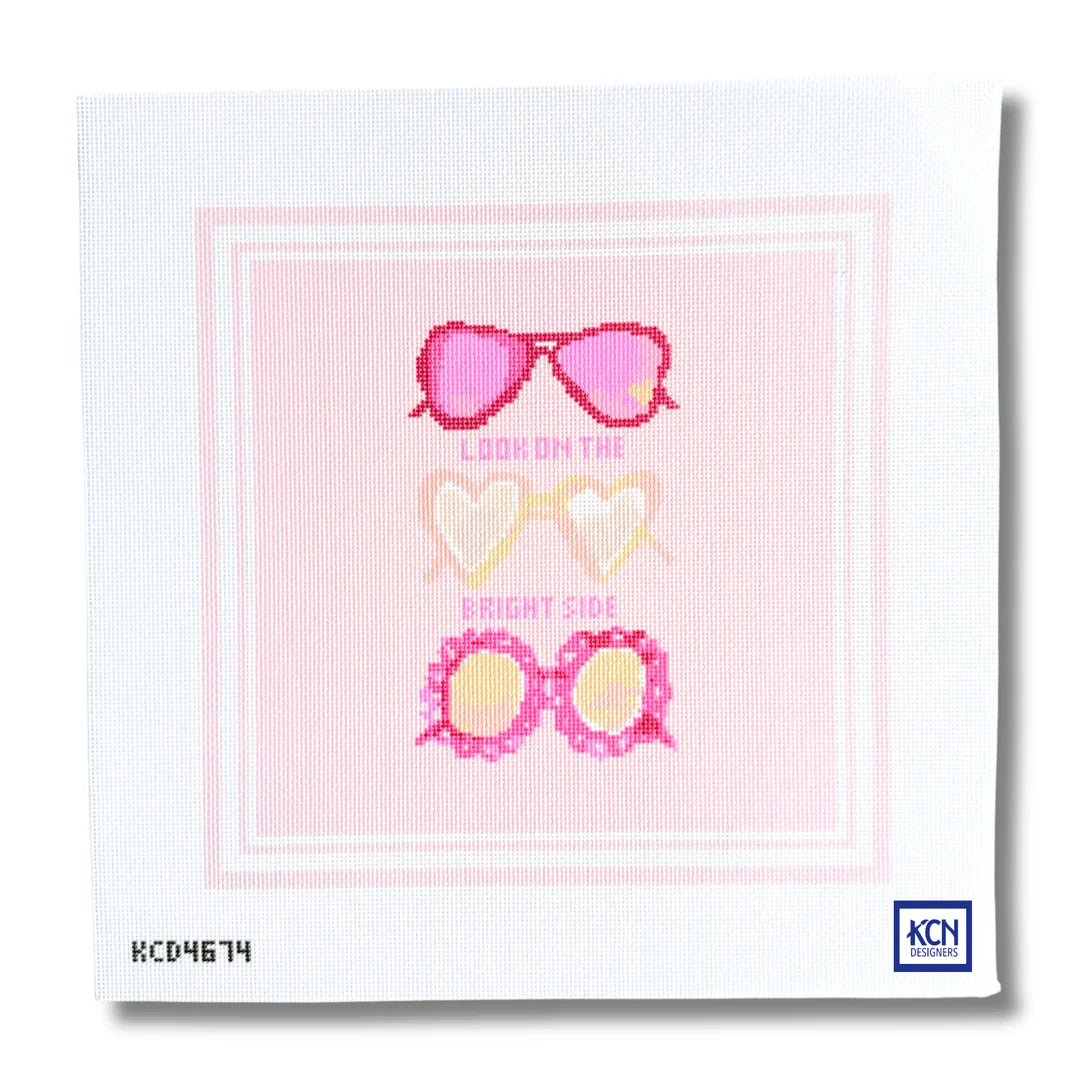 A square needlepoint canvas featuring a pink and white graphic design with three pairs of heart-shaped sunglasses and the text 'LOOK ON THE BRIGHT SIDE'. The canvas shows the KCN Designs brand logo in the bottom right corner.