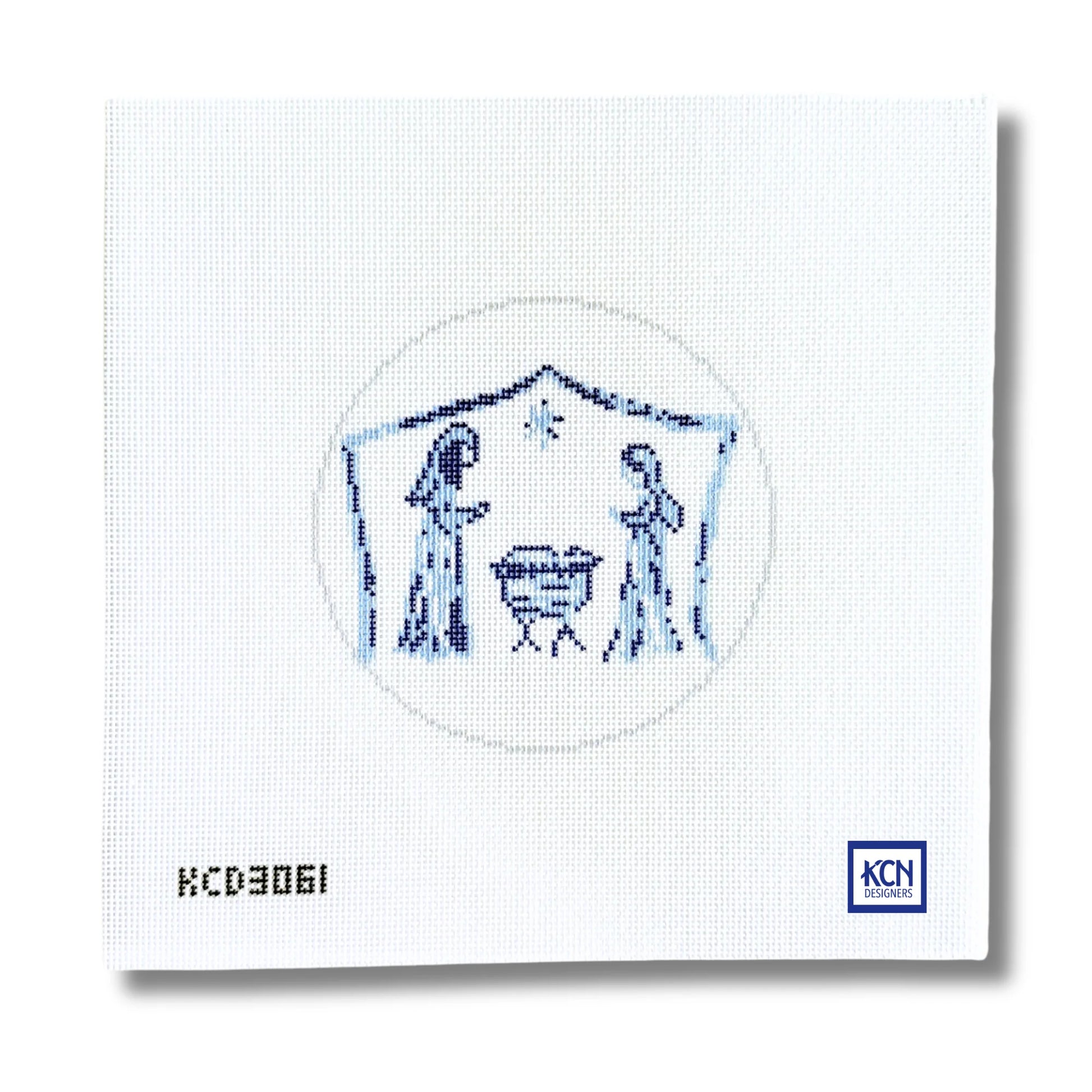 A square white needlepoint canvas featuring a blue embroidered nativity scene with Mary, Joseph, baby Jesus in a manger, and a star. The canvas has the printed code 'KCD3061' in the bottom-left corner and a blue 'KCN' logo in the bottom-right corner.